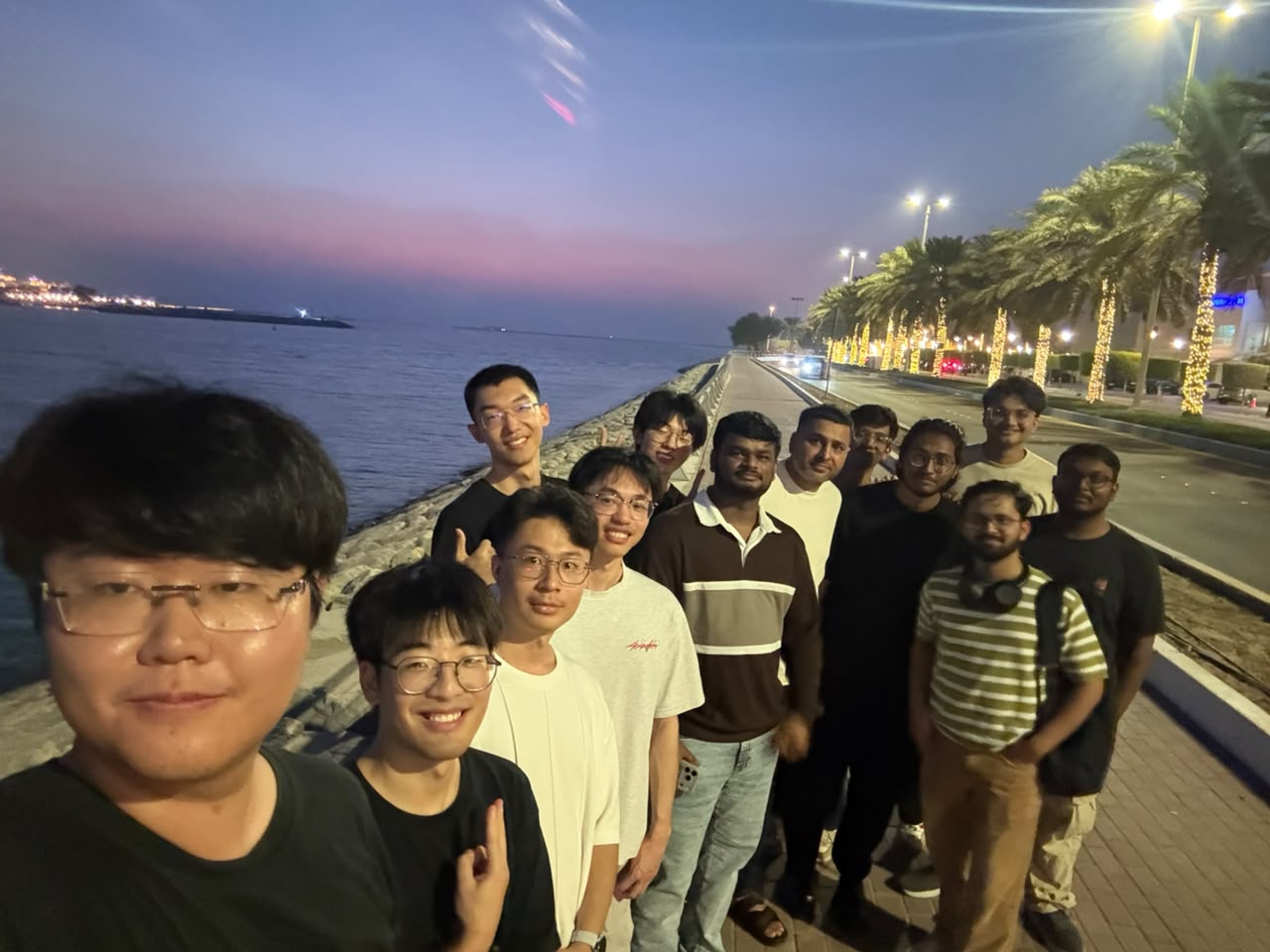 Research team taking a group selfie on a waterfront promenade at dusk.